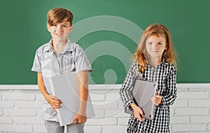 Smiling children hold book with surprising expression against blackboard. School kids friends.