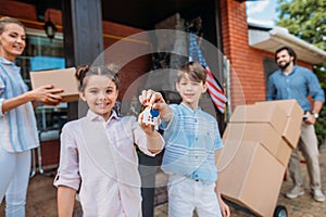 smiling children with keys and parents with cardboard boxes standing at country house moving