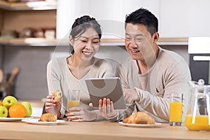 Smiling chinese spouses having breakfast and using tablet