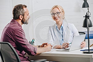 smiling chiropractor pointing at laptop screen during appointment with patient