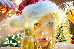 Smiling Christmas girl with red lips. Christmas light. Girl is wearing Santa hat. Concept of holidays. Christmas mood