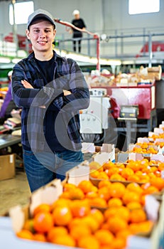 Smiling citrus sorting factory worker standing near boxes of tangerines