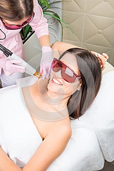 Smiling client cosmetology clinic having Armpit laser hair removal. Beautiful smiling woman client in red glasses having