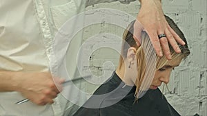 Smiling client sitting in a hair salon while hairdresser is combing her hair. Focus on client