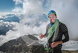 Smiling Climber in a safety harness, helmet, and  on body wrapped climbing rope with picturesque clouds background showing thumb