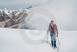 Smiling climber in sunglasses with backpack and trekking poles ascending Mera peak high slopes at 6000m enjoying legendary Mount