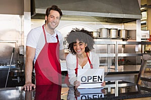 Smiling co-workers posing with open sign