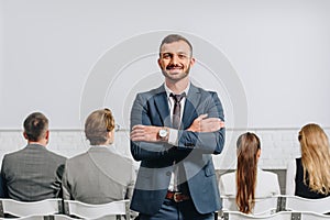 smiling coach with crossed arms looking at camera during business training