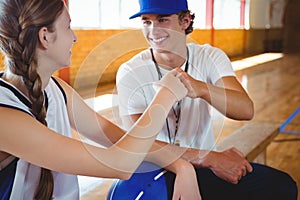 Smiling coach doing fist bump with female basketball player