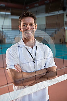 Smiling coach standing behind the net with arms crossed in volleyball court