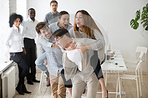 Smiling colleagues laughing playing piggyback ride game in offic