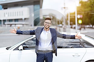 Smiling company leader standing with open arms in front of his car at city street