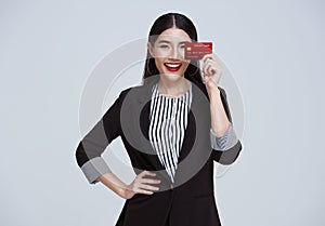 Smiling Confident Asian business woman showing credit card isolated on gray background
