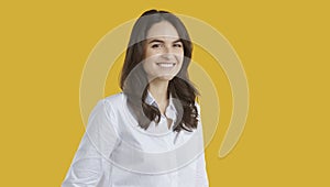 Smiling confident brunette woman in white shirt is posing on yellow background looking at camera.