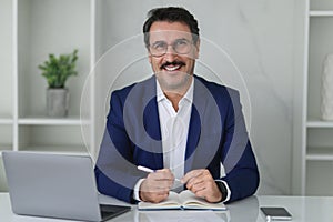 Smiling confident businessman in blue suit writing in a notebook with a laptop and smartphone