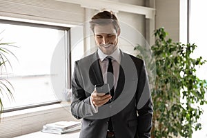 Smiling confident businessman wearing suit looking at phone screen