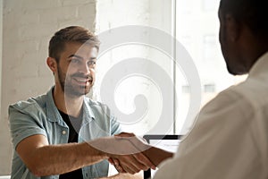 Smiling confident caucasian candidate handshaking african employ