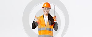 Smiling confident female asian construction engineer, architect in safety helmet, uniform, showing tape measure and