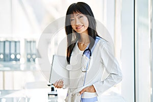 Smiling confident female doctor holding clipboard posing in hospital