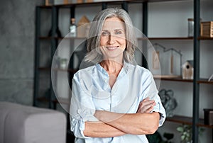 Smiling confident middle aged woman standing arms crossed in office, portrait.