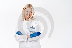 Smiling confident woman doctor, professional standing with arms crossed, wears medical gloves and clinic uniform, white