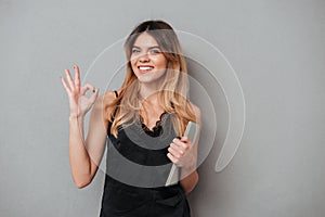Smiling confident woman showing ok gesture and holding tablet computer