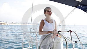 Smiling confident woman steering pleasure yacht on sunny summer day on calm blue sea