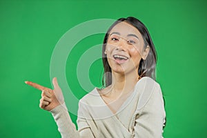 Smiling and confident woman in white is pointing to your product looking at the camera. Isolated on green background