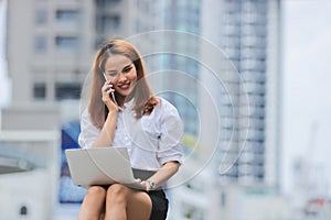 Smiling confident young Asian business woman using laptop for job at outside office