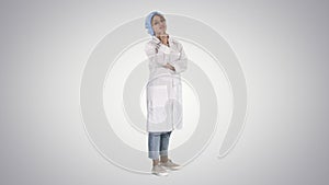 Smiling confident young woman doctor standing with arms crossed over on gradient background.