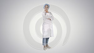 Smiling confident young woman doctor standing with arms crossed over on gradient background.