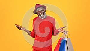 Smiling confused old black man shopaholic in hat, shrugs shoulders with many bags