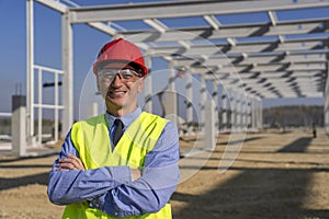 Smiling Construction Manager Standing In Front Of Industrial Building Under Construction