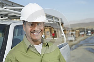 Smiling Construction Worker In Hardhat By Truck On Site