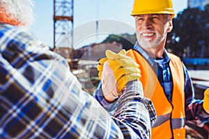 Smiling construction worker in protective uniform shaking hands photo