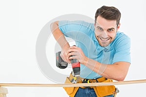 Smiling construction worker using hand drill on wooden plank
