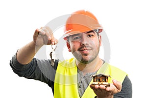 Smiling constructor man presenting wooden house holding keys