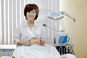 Smiling cosmetician does to patient facial massage