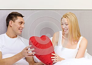 Smiling couple in bed with red heart shape pillow