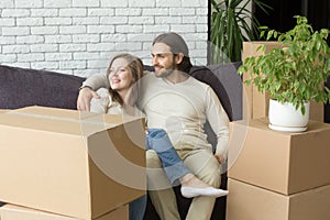 Smiling couple with boxes sitting on sofa embracing, moving day