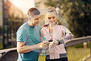 Smiling couple checking time or pulse on heart rate monitor watch - Runners in the park - Man and woman training outside