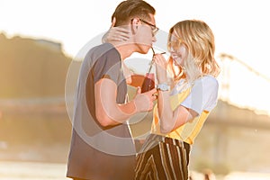 smiling couple drinking beverage with two plastic straws from one bottle on river beach