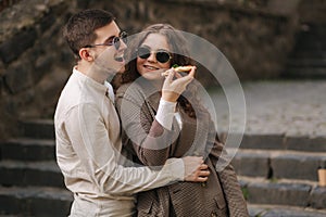 Smiling couple eating pizza outdoors. Man hol pizza box and take slice of vegan pizza. Stylish couple takeway pizza