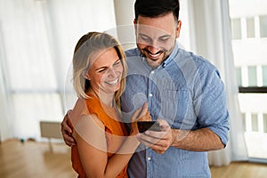 Smiling couple embracing while using a smartphone. People sharing social media on mobile phone.