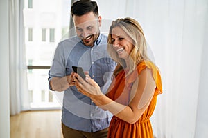 Smiling couple embracing while using a smartphone. People sharing social media on mobile phone.