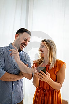 Smiling couple embracing while using a smartphone. People sharing social media on mobile phone.