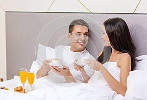 Smiling couple having breakfast in bed in hotel