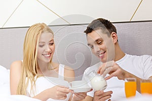 Smiling couple having breakfast in bed in hotel