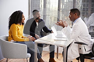 Smiling Couple Having Consultation With Male Doctor In Hospital Office