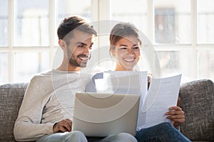 Smiling couple hold paperwork paying bills online